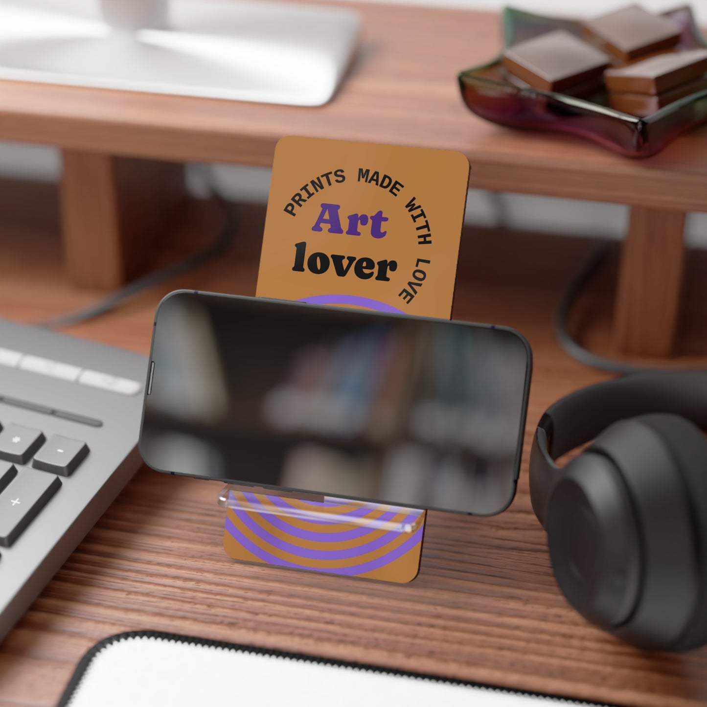 Phone stand with 'Art lover' card on a desk with keyboard, mouse, and headphones.