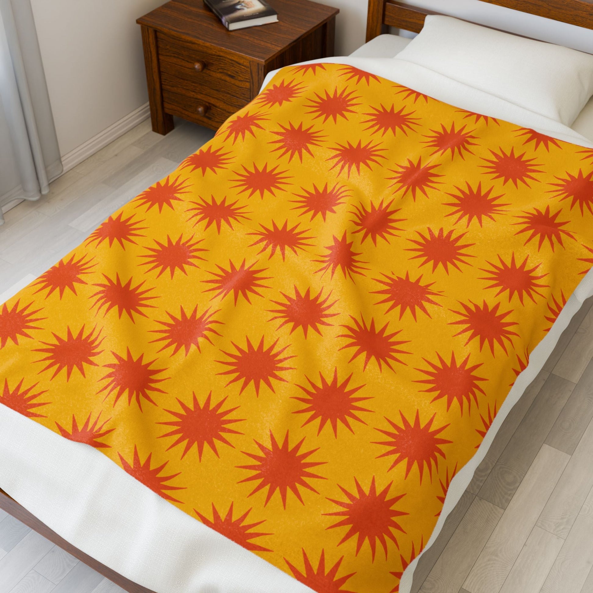 Cozy Velveteen Plush Blanket with vibrant orange starburst pattern on yellow background, spread on bed in modern bedroom setting