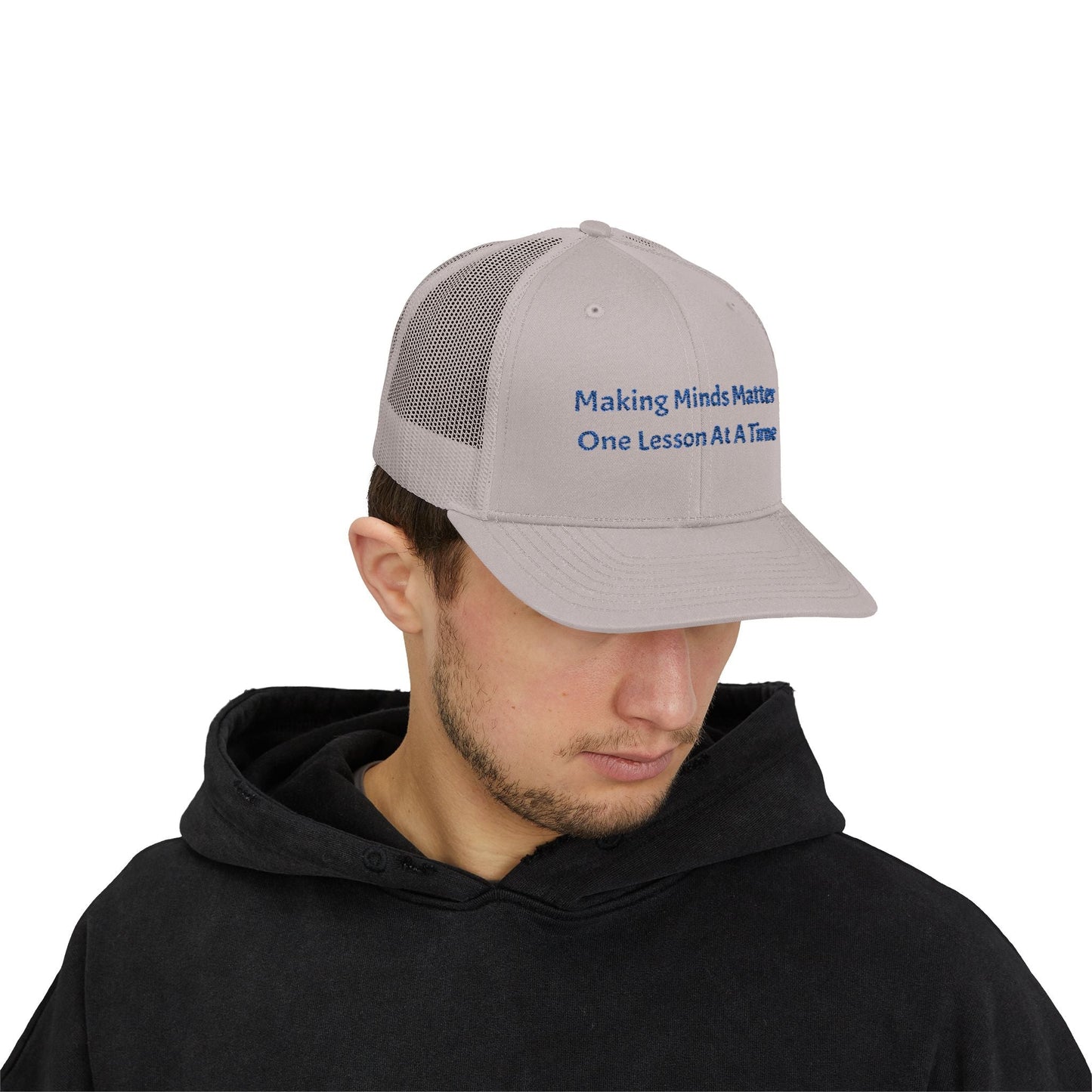 Grey snapback trucker cap with mesh back and embroidered slogan worn by man in black hoodie