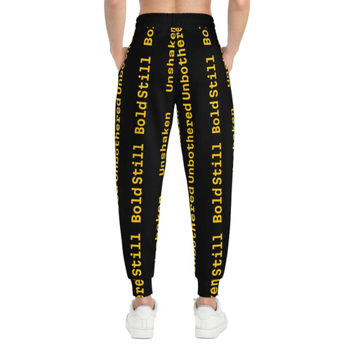 Back view of eco-friendly joggers with black base and bold yellow "Unbothered Unshaken Bold Still" text print, worn with white sneakers