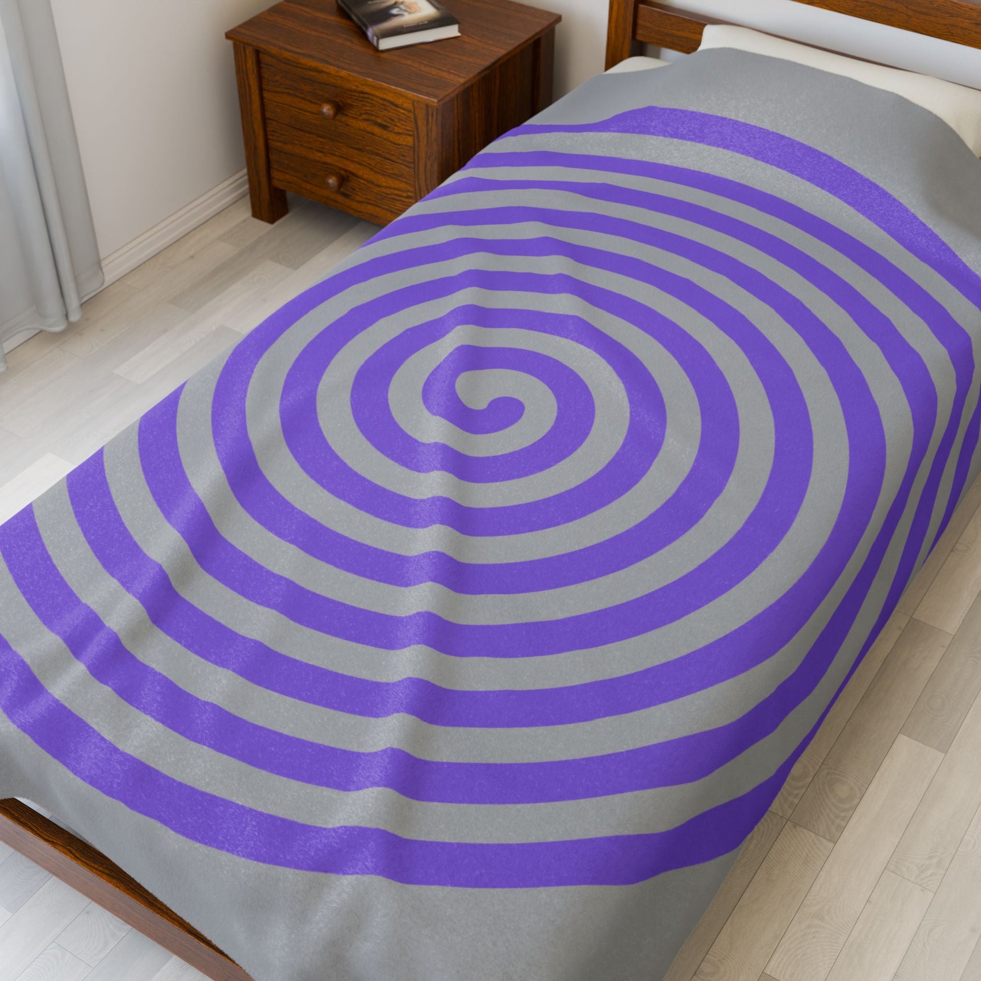 Plush blanket with purple spiral design on gray background on a bed in a cozy bedroom