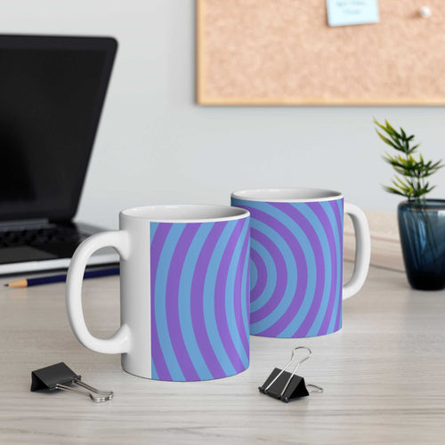 Two vibrant spiral ceramic mugs with blue and purple concentric circle design on a desk near a laptop and plant