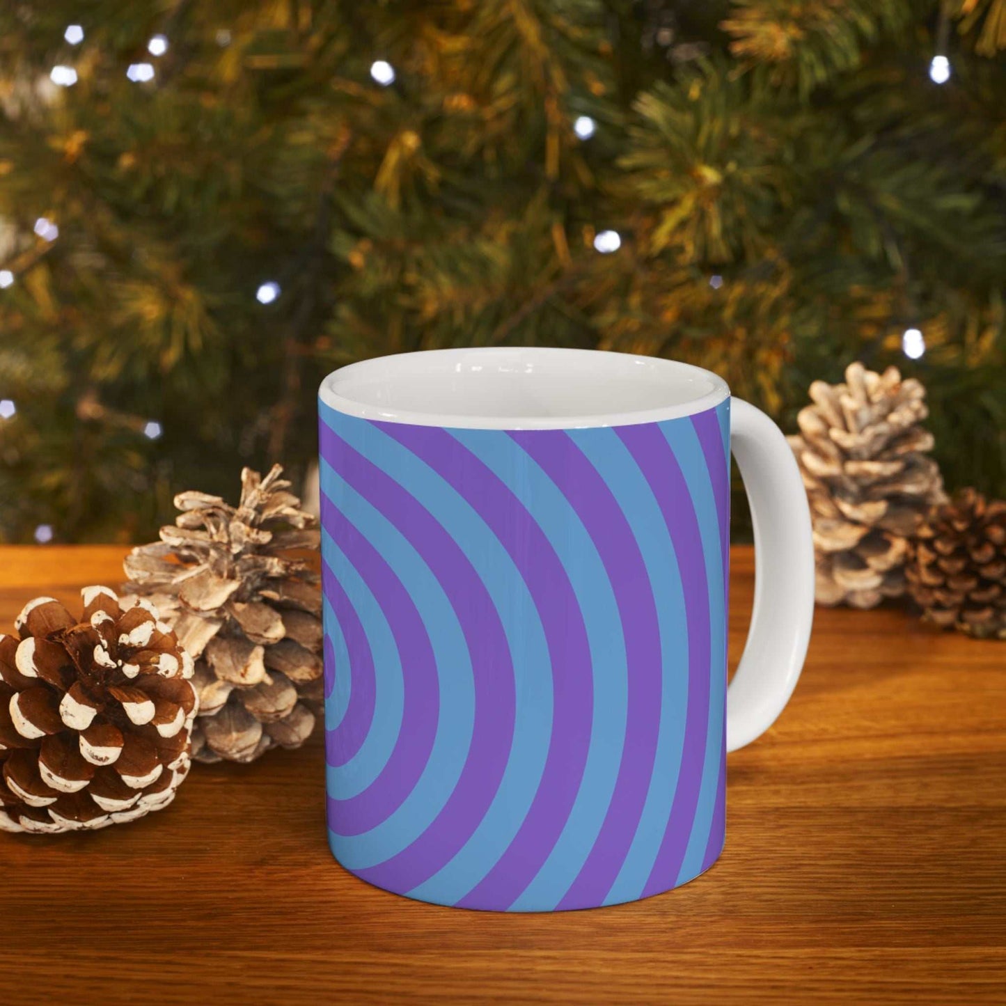 Vibrant Spiral Ceramic Mug with glossy blue and purple spiral design on wooden table with pinecones and blurred festive background