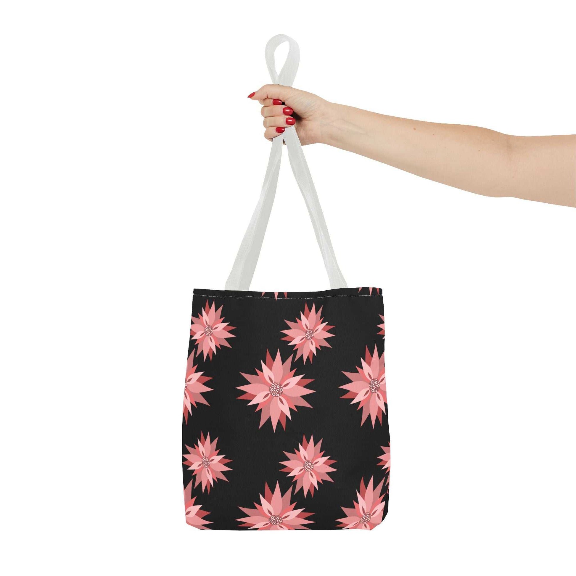 Colorful AOP Tote Bag with pink floral pattern and white handles held by hand against white background