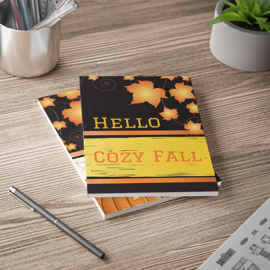 Cozy Fall Notebook with autumn leaves design lying on wooden desk with pen and plant