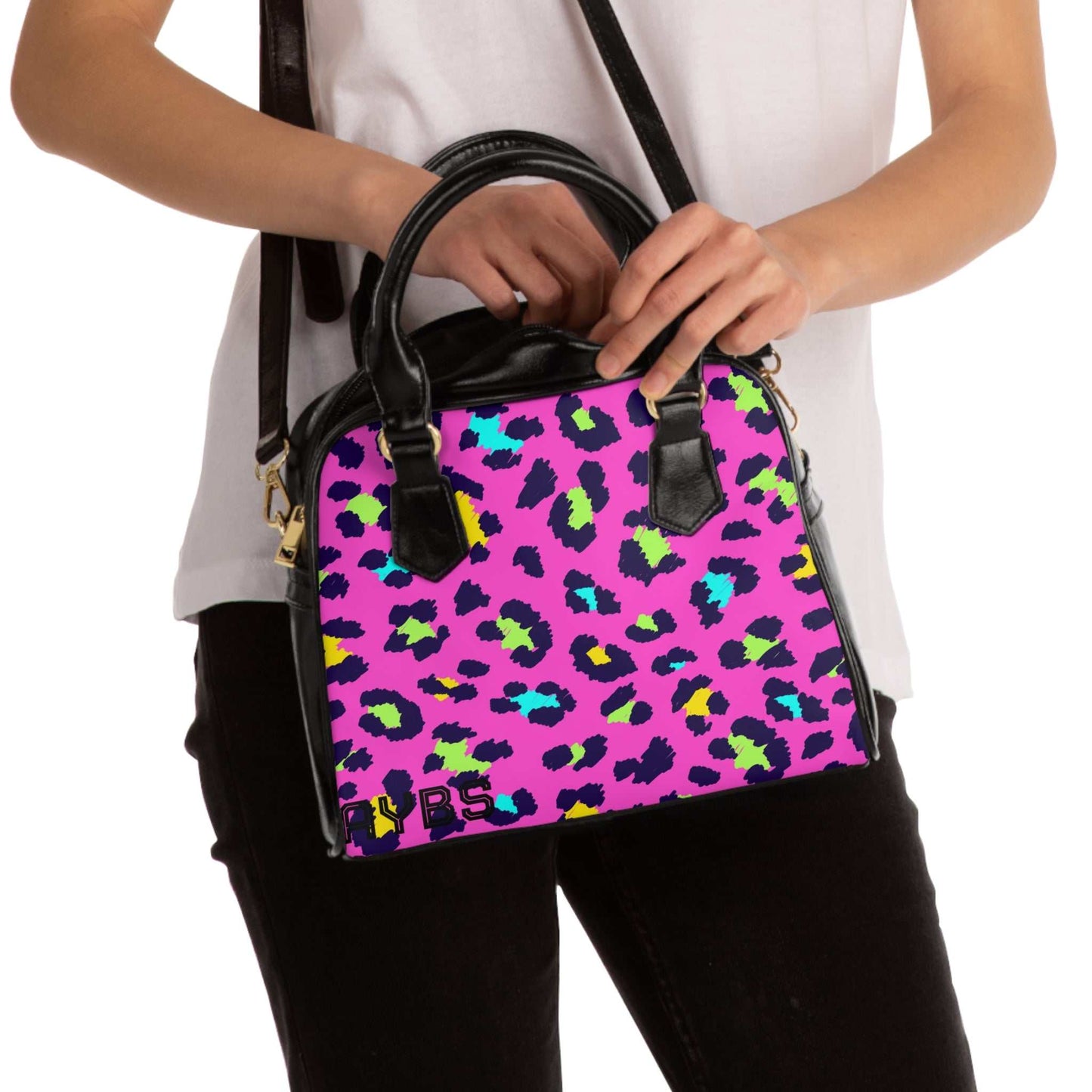 Woman holding vibrant leopard print shoulder handbag with adjustable strap and black handles