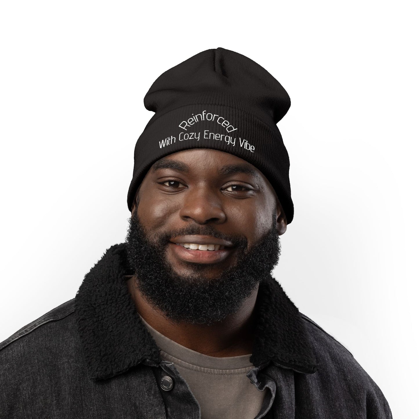 Black knit beanie with embroidered "Reinforced with Cozy Energy Vibe" worn by smiling man with beard, cozy winter accessory