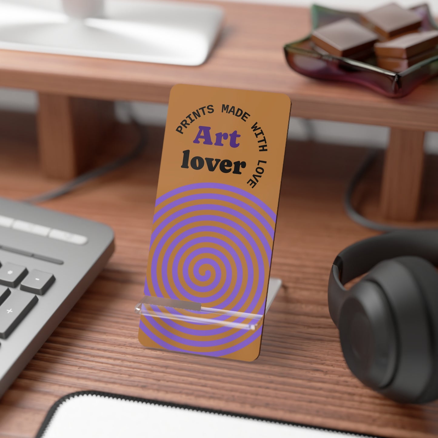 Phone stand with purple spiral design and text on a desk with computer and headphones.