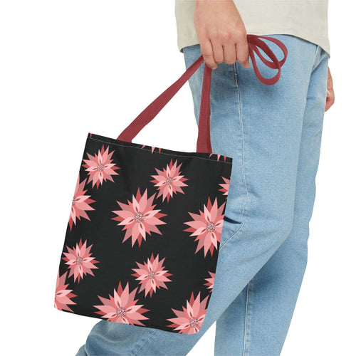 Colorful AOP Tote Bag with pink floral design and red handles, held by person in jeans