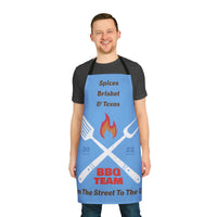 Man wearing blue apron with BBQ team design and black straps standing smiling