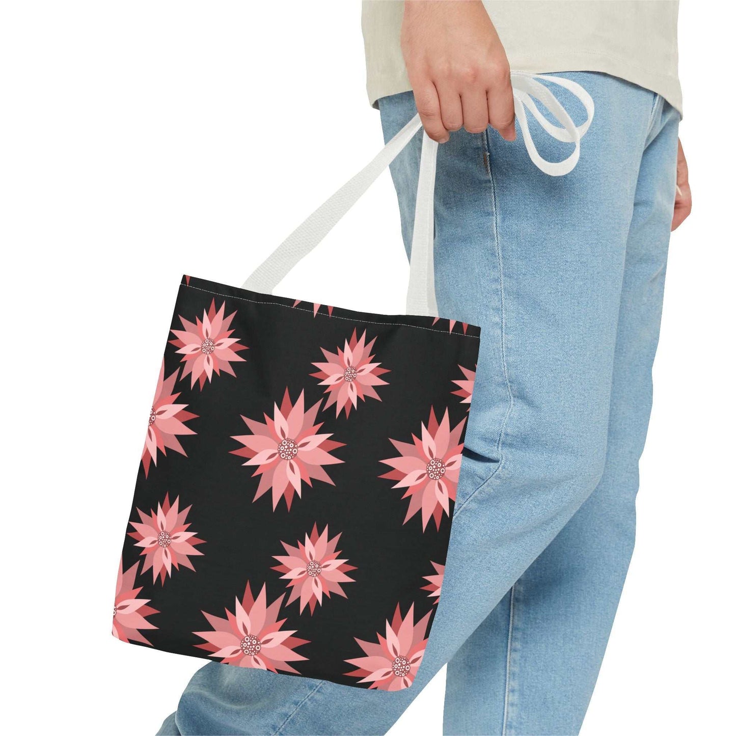 person holding colorful AOP tote bag with pink floral pattern and white handles against black background