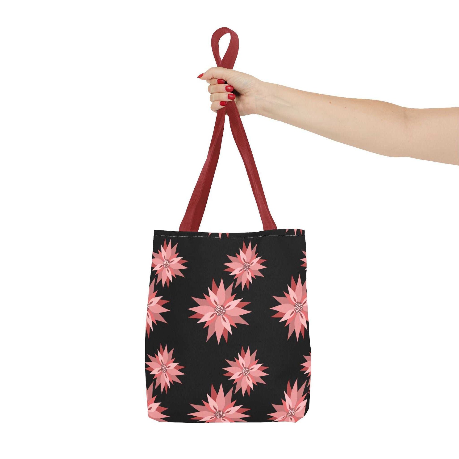 Colorful AOP Tote Bag with pink floral pattern and red handles held by hand, reusable shopping bag