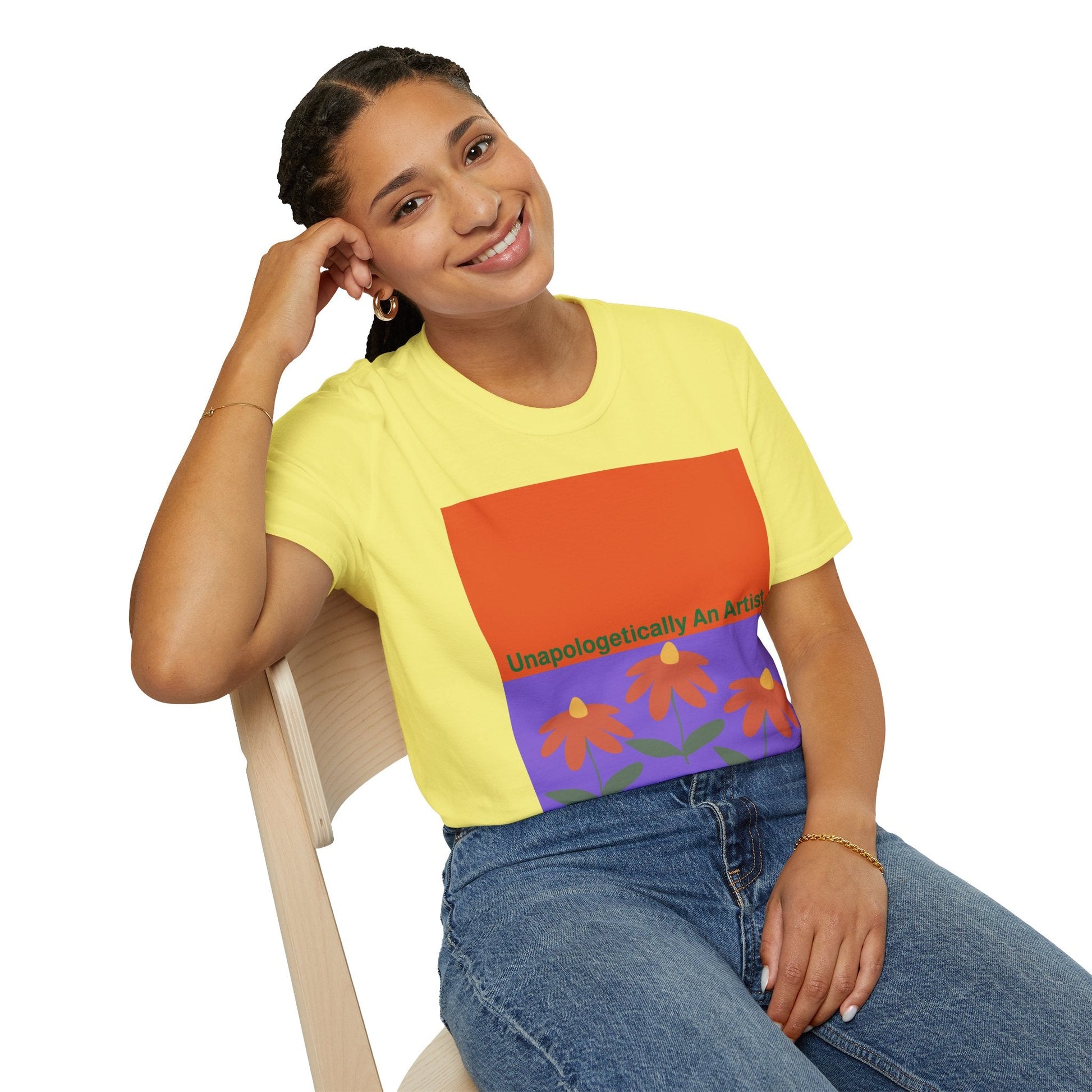 Smiling woman wearing yellow Unapologetically An Artist T-Shirt with floral graphic and casual jeans sitting on wooden chair
