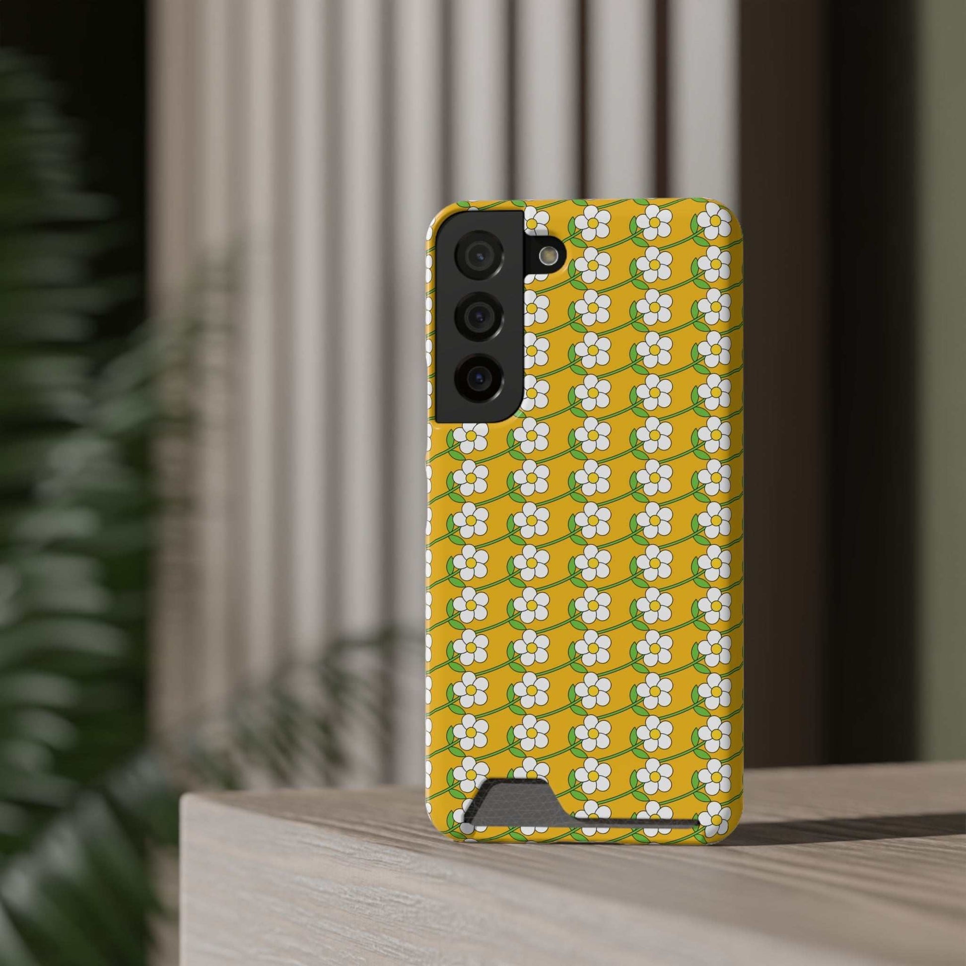 Yellow floral phone case with white daisy pattern and built-in card holder on smartphone