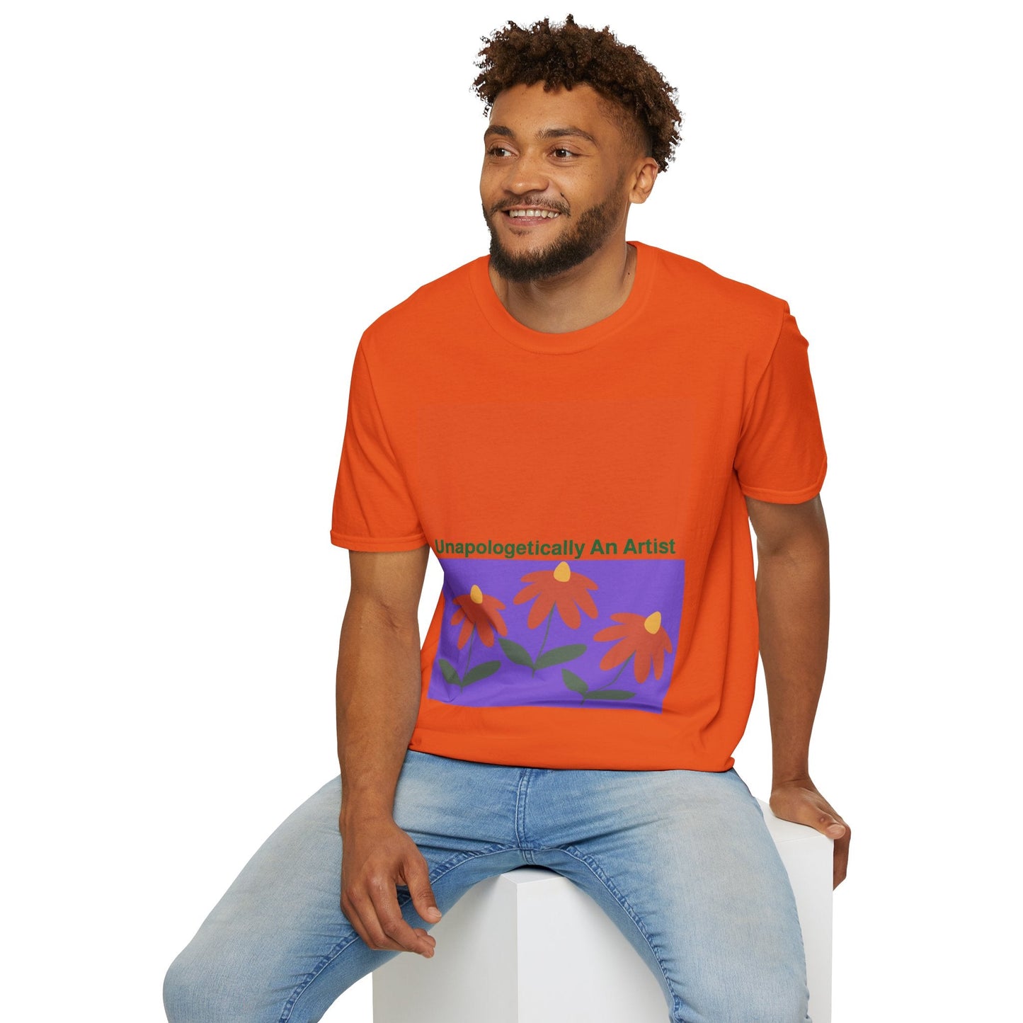 Man wearing bright orange Unapologetically An Artist T-Shirt with floral design sitting on white block