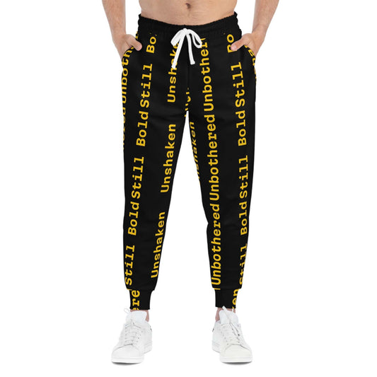 Eco-friendly black joggers with bold yellow "Unbothered Unshaken Bold Still" text, adjustable white drawstring, side pockets, and tapered ankle cuffs.