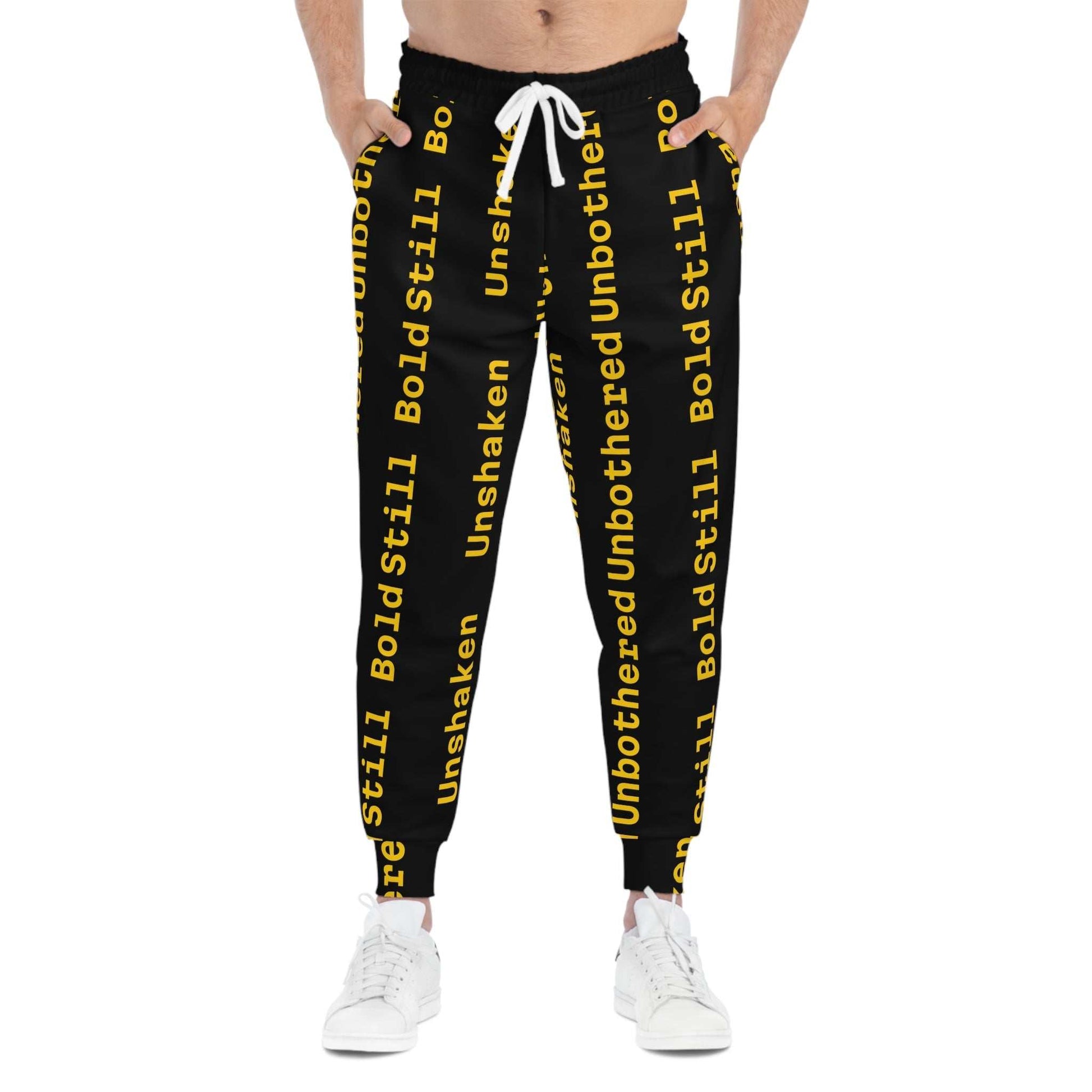Eco-friendly black joggers with bold yellow "Unbothered Unshaken Bold Still" text, adjustable white drawstring, side pockets, and tapered ankle cuffs.