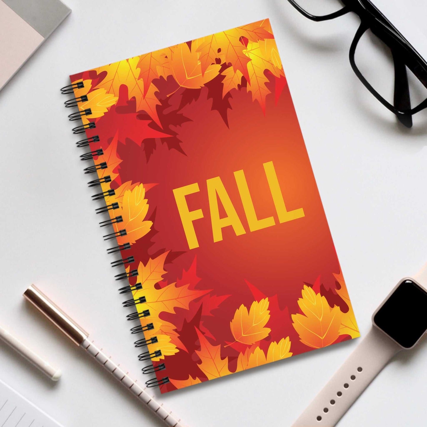 Fall Holiday Spiral Notebook with vibrant autumn leaves design and semi-gloss laminated cover on desk with pen, glasses, and smartwatch